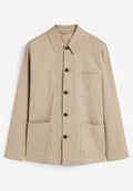 Beige Jacke mit Kragen, langen Ärmeln, schwarzen Knöpfen, zwei vorderen Taschen und einer Brusttasche; aus Baumwolle und schlichtem Design.