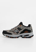 Grau-schwarzer und orangefarbener Skechers-Sneaker mit Mesh- und Wildlederpaneelen, dicker Sohle und Schnürdesign, seitlich auf weißem Hintergrund gezeigt.