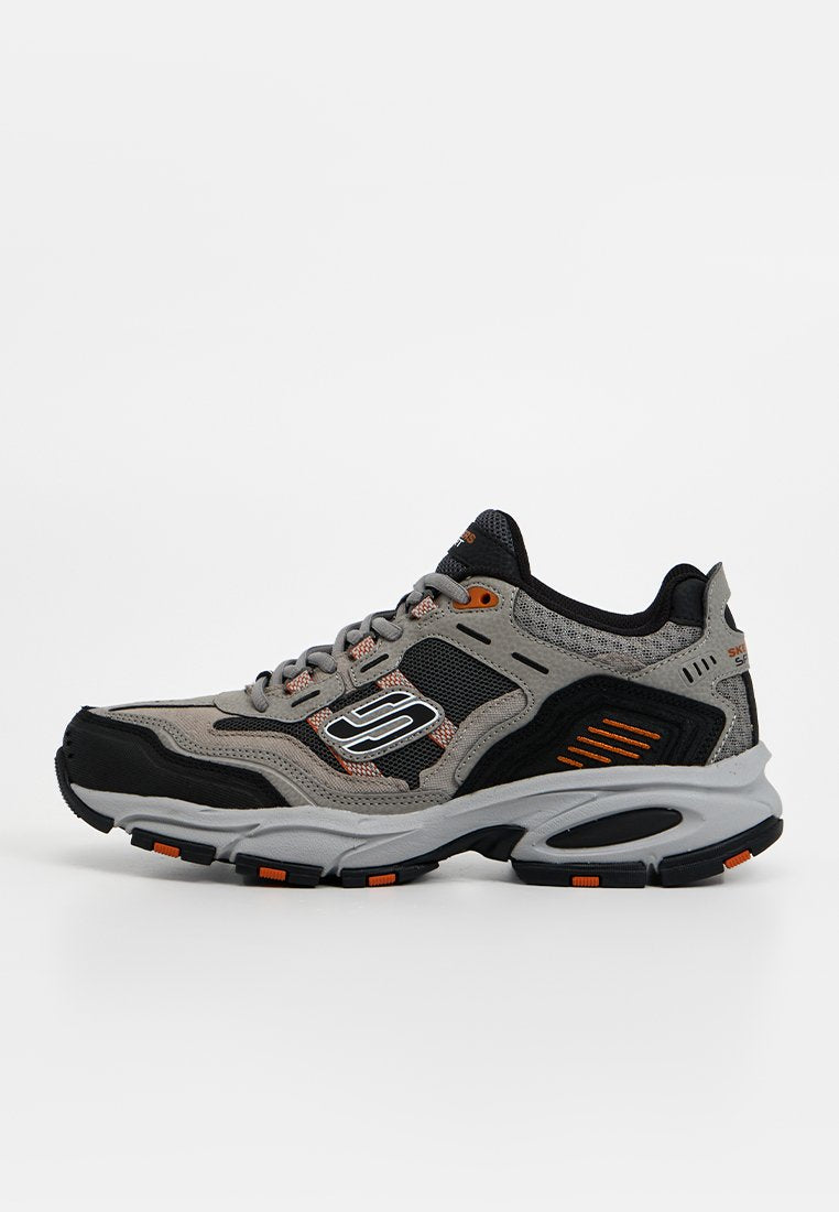 Grau-schwarzer und orangefarbener Skechers-Sneaker mit Mesh- und Wildlederpaneelen, dicker Sohle und Schnürdesign, seitlich auf weißem Hintergrund gezeigt.