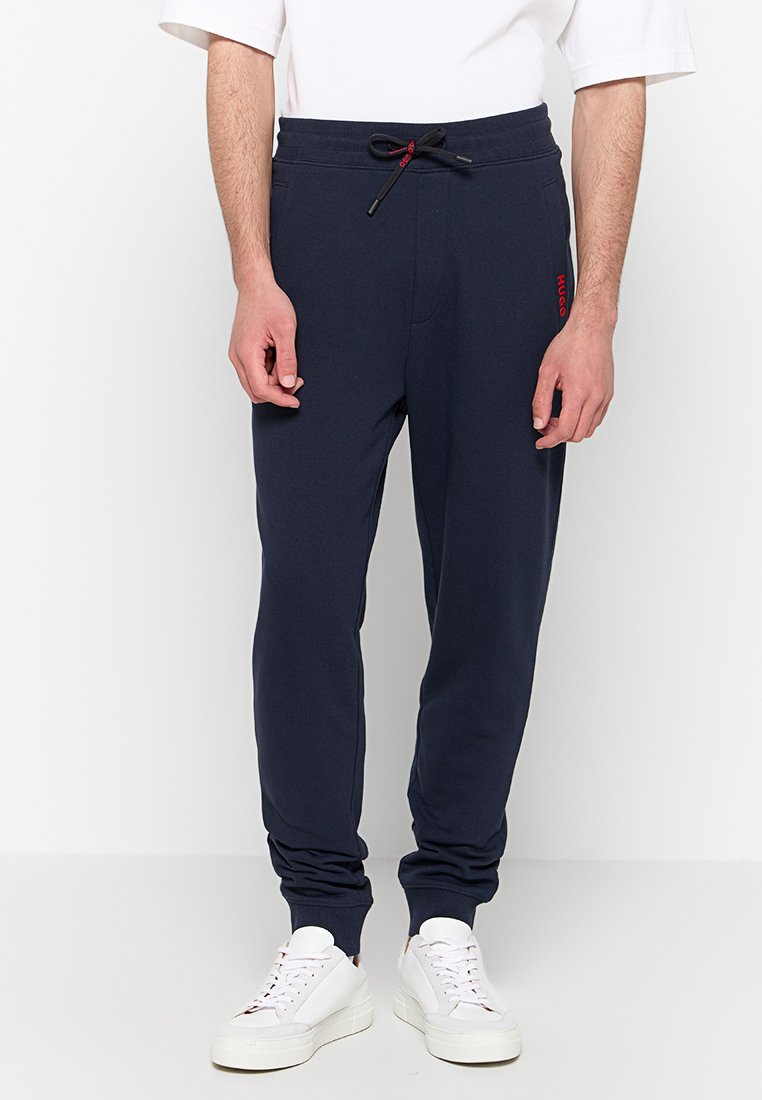 Marineblaue Sweatpants mit Kordelzugbund, gerippten Bündchen und rotem Logoakzent am Oberschenkel, aus einem weichen, dehnbarem Stoff.