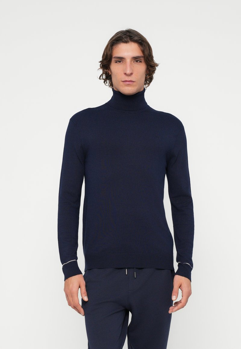 Marineblauer Rollkragenpullover aus Strickstoff mit langen Ärmeln, figurbetontem Schnitt, feiner Rippstruktur und kontrastierendem Besatz an den Bündchen.