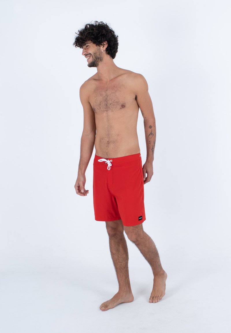 Rote Badeshorts aus leichtem Stoff, mit einem weißen Kordelzug, Seitentaschen und einem kleinen Markenlogo am Saum.