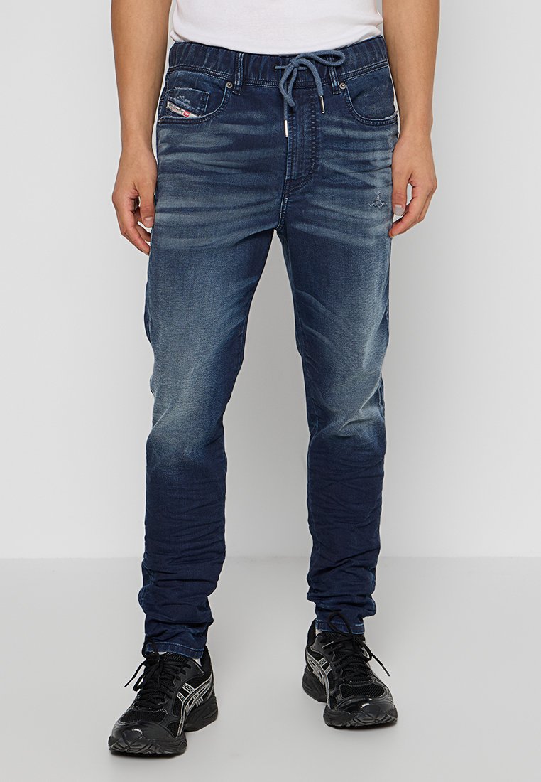 Dunkelblaue Denim-Jogger mit einem verblassten Effekt, Kordelzugbund, seitlichen Taschen und schmal zulaufenden Beinen, kombiniert mit schwarzen Sportschuhen.