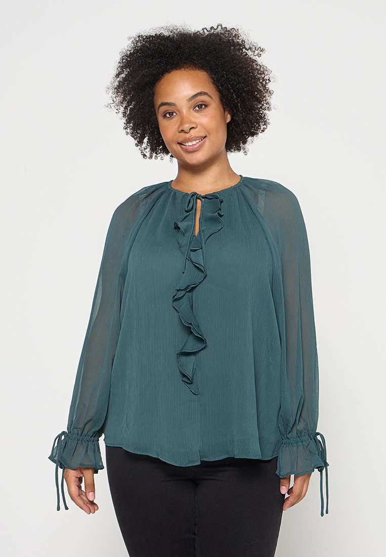 Tealfarbige, transparente Bluse mit rüschente Front, rundem Halsausschnitt und Kordelzugmanschetten. Mit langen Ärmeln und einem lässigen Schnitt.