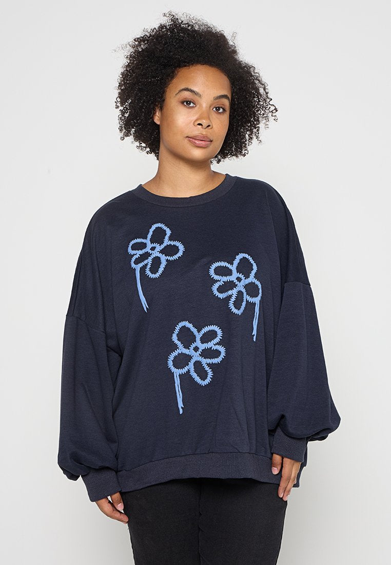 Navy Oversize-Sweatshirt mit hellblauer Blumenstickerei. Weicher Stoff mit lockerer Passform und langen Ärmeln. Gerippter Saum und Bündchen.