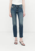 Frau in hellen, mittelhohen, blauen Straight-Leg-Jeans und schwarzen, schlichten, hohen Sandalen, die vor einem weißen Hintergrund steht.