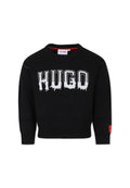 Schwarzer Strickpullover mit Rundhalsausschnitt. Verfügt über ein weißes, tropfendes "HUGO"-Logo auf der Brust und ein rotes Logo-Label am Ärmel.