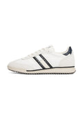 Weißer Sportschuh mit schwarzen und cremefarbenen Streifen, Obermaterial aus glattem Leder, Gummisohle und strukturiertem Fersenakzent. Schnürsenkel und Logo an der Seite.