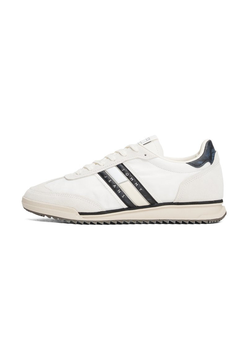 Weißer Sportschuh mit schwarzen und cremefarbenen Streifen, Obermaterial aus glattem Leder, Gummisohle und strukturiertem Fersenakzent. Schnürsenkel und Logo an der Seite.