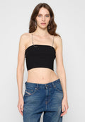 Frau mit langen braunen Haaren, die ein schwarzes trägerloses Crop-Top mit Kettenriemen und blaue lässige Jeans trägt, vor einem schlichten Hintergrund.