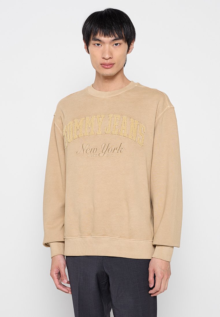 Beiger Sweatshirt mit Rundhalsausschnitt, auf der Brust mit "TOMMY JEANS" in Gold gestickt, aus weichem Stoff und mit lässiger Passform.