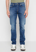 Mann trägt blaue Jeans und weiße Sneaker mit grünen Streifen und steht vor einem schlichten hellen Hintergrund.