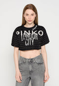 Schwarzes, kurzes T-Shirt mit weißem Drucktext "PINKO LONDON CITY", das ein Nietenmuster und einen runden Ausschnitt aufweist. Kombiniert mit grauen Jeans.