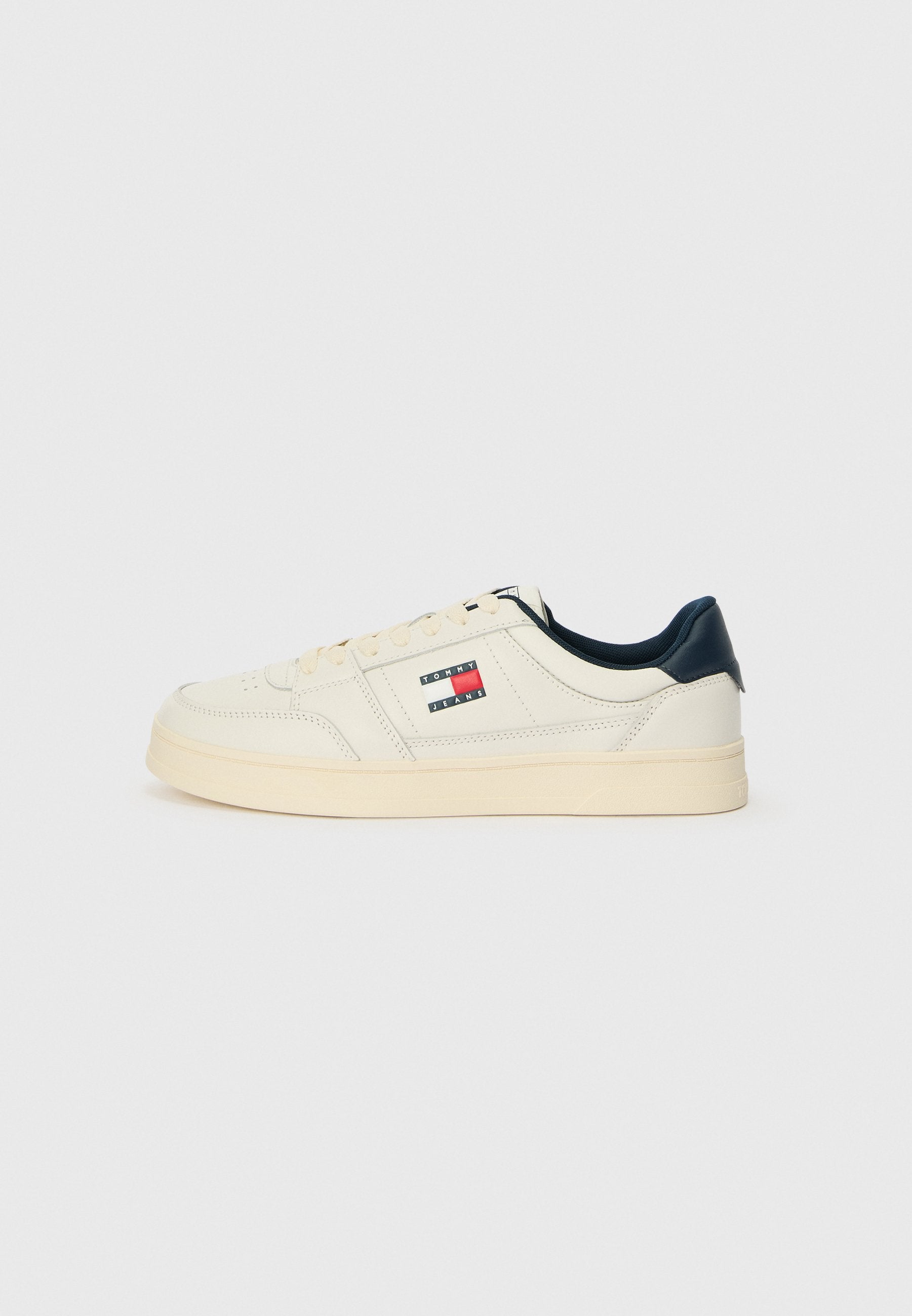 Sneaker aus cremigem weißen Leder mit einer navyblauen Ferse und Zunge, versehen mit einem Logo-Patch in Rot, Weiß und Blau an der Seite.