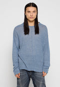 Hellblauer, gerippter Pullover mit langen Ärmeln, lockerer Passform, tiefen Schultern und rohem Saum. Kombiniert mit ausgebleichten blauen Jeans.