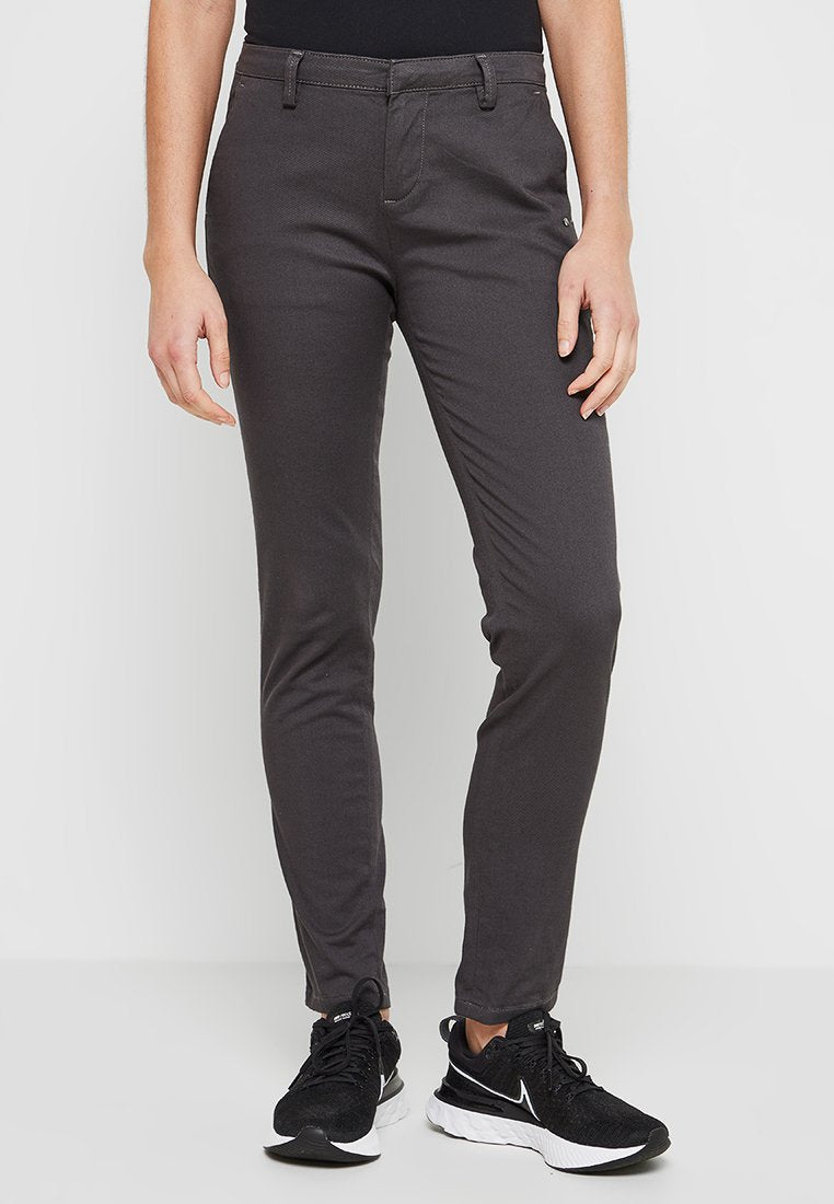 Graue Stretch-Hosen mit schlanker Passform, ausgestattet mit schrägen Seitentaschen und einer glatten Textur. Kombiniert mit schwarzen Sportschuhen.