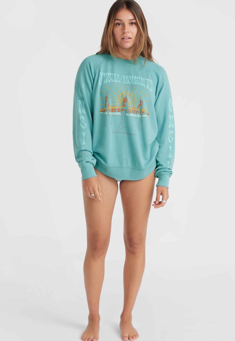 Hellblauer, oversized Sweatshirt mit Bündchen an den Ärmelenden und am Saum. Es zeigt einen grafischen Druck mit einer Sonne, Figuren und dem Wort "California" in Orange und Weiß.