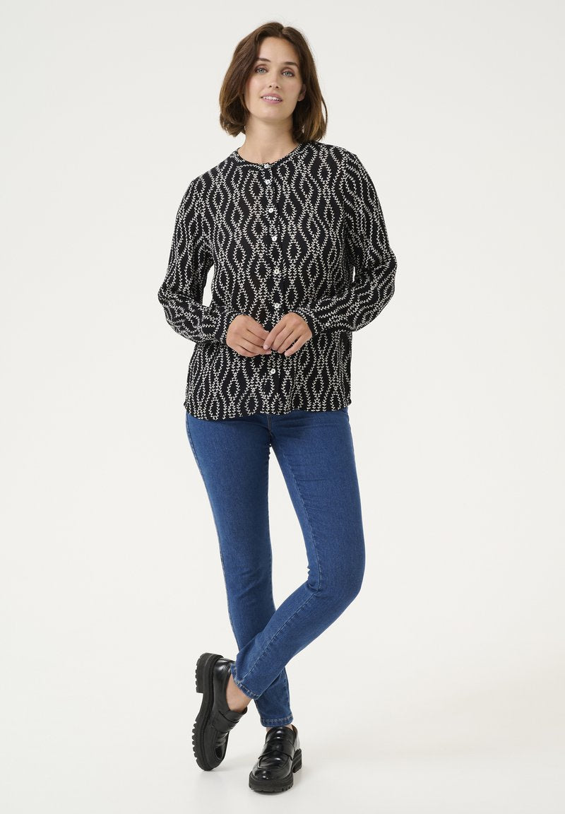 Schwarz-weiße gemusterte Bluse mit langen Ärmeln, kombiniert mit blauen Jeans und schwarzen Schuhen, die einen entspannten Schnitt zeigt.