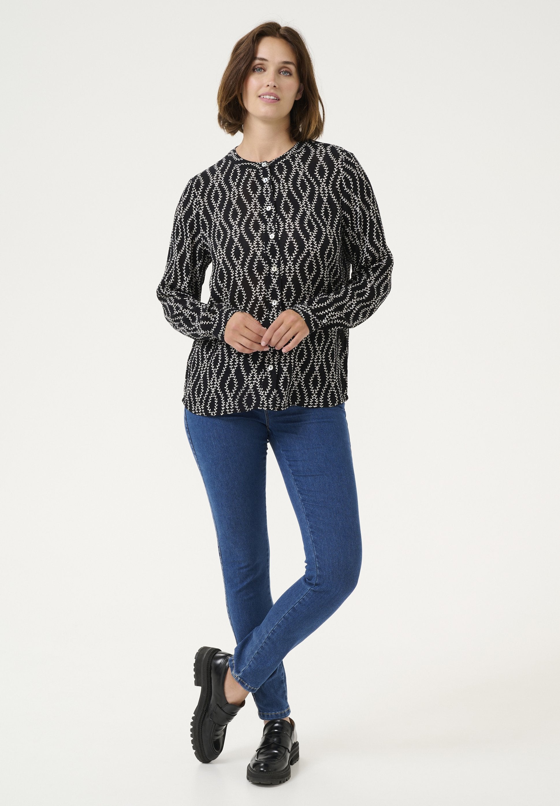 Schwarz-weiße gemusterte Bluse mit langen Ärmeln, kombiniert mit blauen Jeans und schwarzen Schuhen, die einen entspannten Schnitt zeigt.