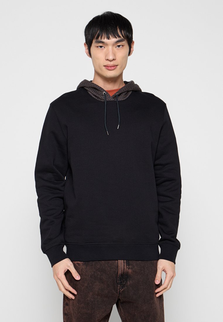 Schwarzer Pullover mit strukturiertem braunem Kapuzenfutter und Kordelzug. Glatter Stoff, gerippte Bündchen und Saum. Modell zeigt eine gerade Passform.