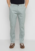 Mann trägt hellgraue Slim-Fit-Hose, schwarzes Hemd und braune Sneakers, steht mit Händen in den Taschen.
