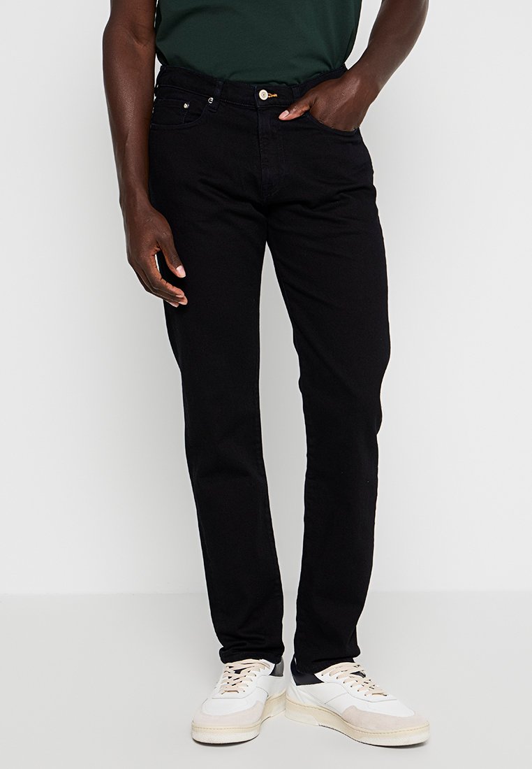 Schwarze Jeans aus Denim mit einer slim fit Passform, ausgestattet mit einem Fünf-Taschen-Design, einem goldenen Knopfverschluss und subtilen Stickdetails. Kombiniert mit weißen Sneakers.