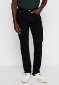 Schwarze Jeans aus Denim mit einer slim fit Passform, ausgestattet mit einem Fünf-Taschen-Design, einem goldenen Knopfverschluss und subtilen Stickdetails. Kombiniert mit weißen Sneakers.