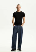 Schwarzes T-Shirt mit kurzen Ärmeln, kombiniert mit weitlegigen Denim-Jeans. Die Jeans sind dunkelblau mit sichtbaren Nähten und einer lockeren Passform. Schwarze Schuhe runden das Outfit ab.