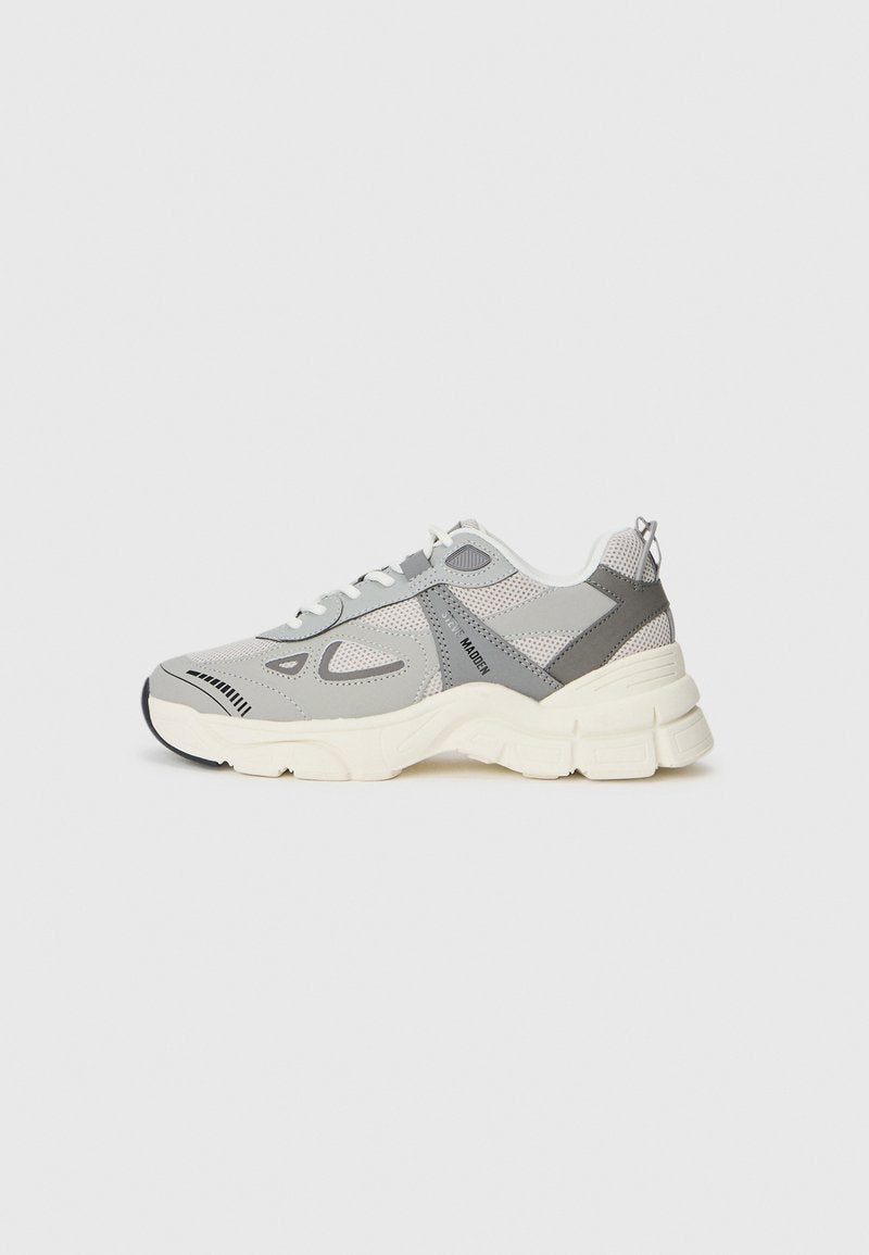 Graue Mesh-Sneaker mit weißen und schwarzen Akzenten. Verfügbar mit einer dicken Sohle, Schnürsystem und einem ausgeprägten Seitenpaneeldesign. Strukturierte Oberflächen im gesamten Schuh.