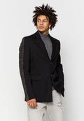 Schwarzer Blazer mit einer strukturierten grauen Wollärmel. Mit einem Reverskragen und zwei Fronttaschen. Getragen über einem grauen Rollkragenpullover.