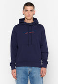 Junger Mann in einem navyblauen Kapuzenpulli mit Fronttasche und blauen Jeans, der vor einem schlichten weißen Hintergrund steht.
