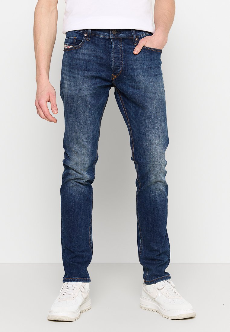 Dunkelblaue Denim-Jeans mit schmalem Schnitt, verblassten Stellen, kontrastierenden Nähten und Fünf-Taschen-Design, kombiniert mit weißen Sneakers.