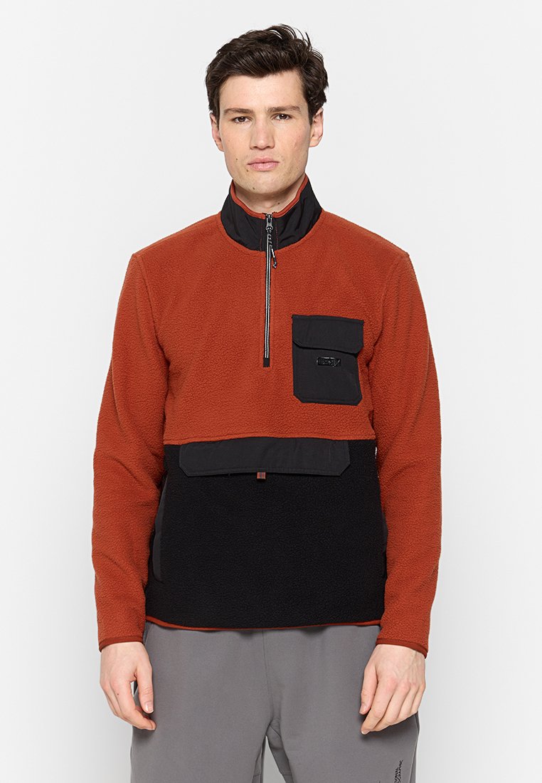 Fleece-Pullover mit Halbe-Zip-Design, bestehend aus einem orangefarbenen Oberteil und einem schwarzen unteren Abschnitt, sowie einer Brusttasche mit Klappe. Strukturierter Stoff.