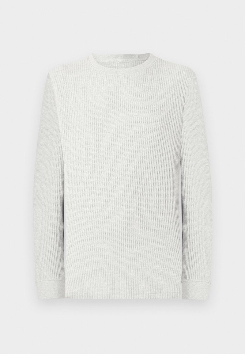 Langärmliges, hellgraues Waffelstrick-Shirt mit Rundhalsausschnitt, gerippten Bündchen und strukturierter Stoffstruktur vor einem einfarbigen Hintergrund.