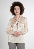 Beige Satinbluse mit einer gebundenen Schleife am Ausschnitt, langen Ärmeln mit Knopfdetails und einem dezenten Glanz. Hahnentritt-Musterhose.