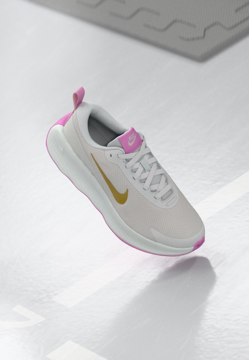 Hellgraue Sportschuh mit pinken Akzenten und einem goldenen Swoosh-Logo. Verfügt über ein Obermaterial aus Mesh, eine gepolsterte Zunge und eine strukturierte Sohle.