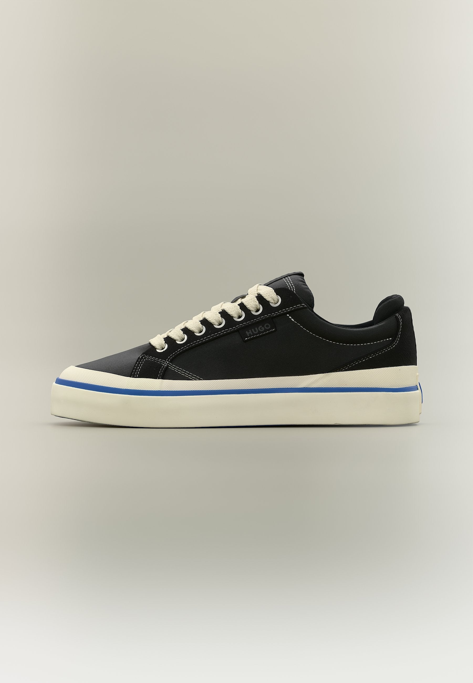Schwarzer Sneaker in niedriger Ausführung mit weißen Schnürsenkeln, weißer Sohle mit blauem Streifen und "HUGO" Logo an der Seite vor schlichtem Hintergrund.