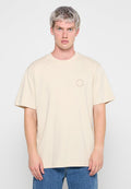 Beige Baumwoll-T-Shirt mit Rundhals und kurzen Ärmeln. Verfügt über ein kleines kreisförmiges Logo, das auf der linken Seite aufgedruckt ist. Getragen mit blauen Denim-Jeans.
