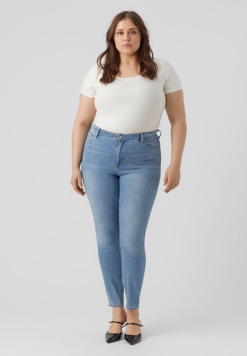 Hellblaue Skinny-Jeans mit hoher Taille, subtilen Used-Effekten und einer glatten Denim-Oberfläche, kombiniert mit einem figurbetonten weißen Oberteil.