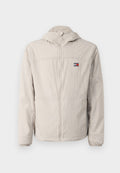Helle beige windbreaker-Jacke mit Reißverschluss und Kapuze, elastischen Bündchen, seitlichen Taschen und einem kleinen Tommy Jeans-Logo auf der Brust.