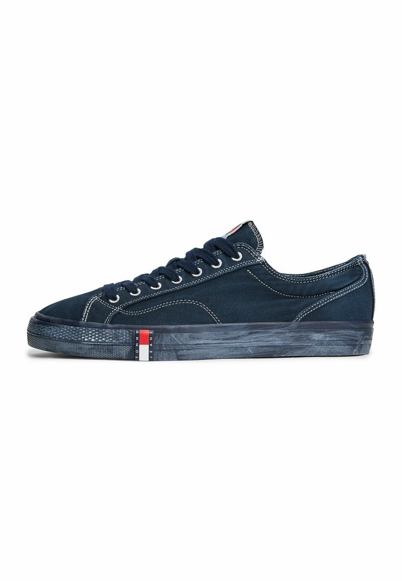 Niedriger, marineblauer Canvas-Sneaker mit weißen Nähten, marineblauen Schnürsenkeln und einer strukturierten schwarzen Sohle mit einem rot-weiß-blauen Logo-Streifen.