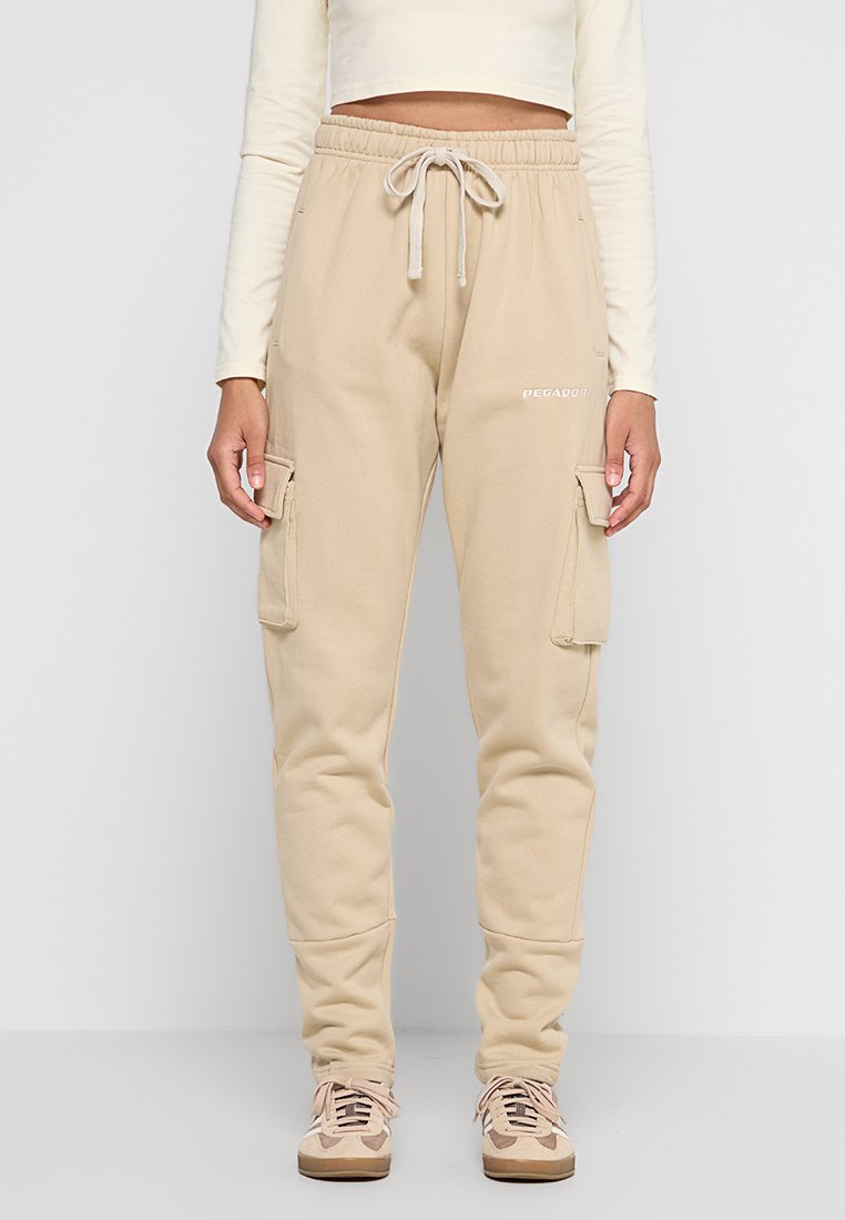 Beige Cargo-Sweatpants mit weichem Material, einer Zugbandtaille und Seitentaschen. Mit weißem Branding am Oberschenkel.