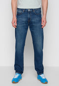 Dunkelblaue Jeans mit geradem Bein, fünf Taschen und kontrastierenden orangefarbenen Nähten, getragen mit blauen Sportschuhen.