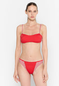 Frau in einem roten Bikini mit gestreiften Trägern und Seitenpanelen, die vor einem schlichten weißen Hintergrund steht und nach vorne schaut.