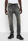 Graue Jeans aus Denim mit einem verblassten Finish, beschädigten Akzenten auf der Vorderseite, elastischem Kordelzug und Kontrastnähten. Kombiniert mit schwarzen Sneakers.