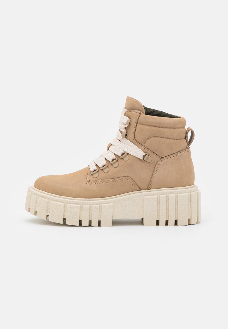 Tan-farbene Wildleder-Ankle-Boots mit weißen Schnürsenkeln, dicker hellcremefarbener Sohle, abgerunderter Zehenpartie und einer Schlaufe an der Rückseite; strukturierte Oberfläche mit tonal abgestimmten Nähten.