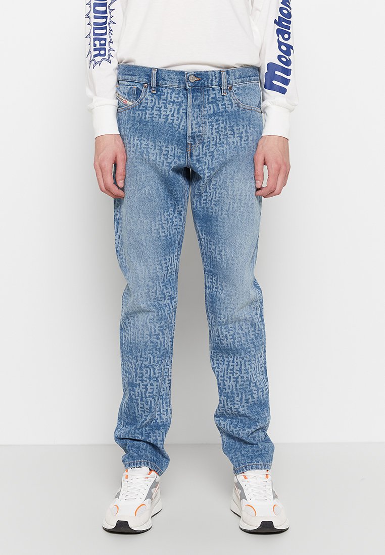 Helle blaue Jeans aus Denim mit einem strukturierten Muster, fünf Taschen, geradem Bein und subtiler Ausbleichung. Getragen mit weißen Turnschuhen und einem Langarmshirt.