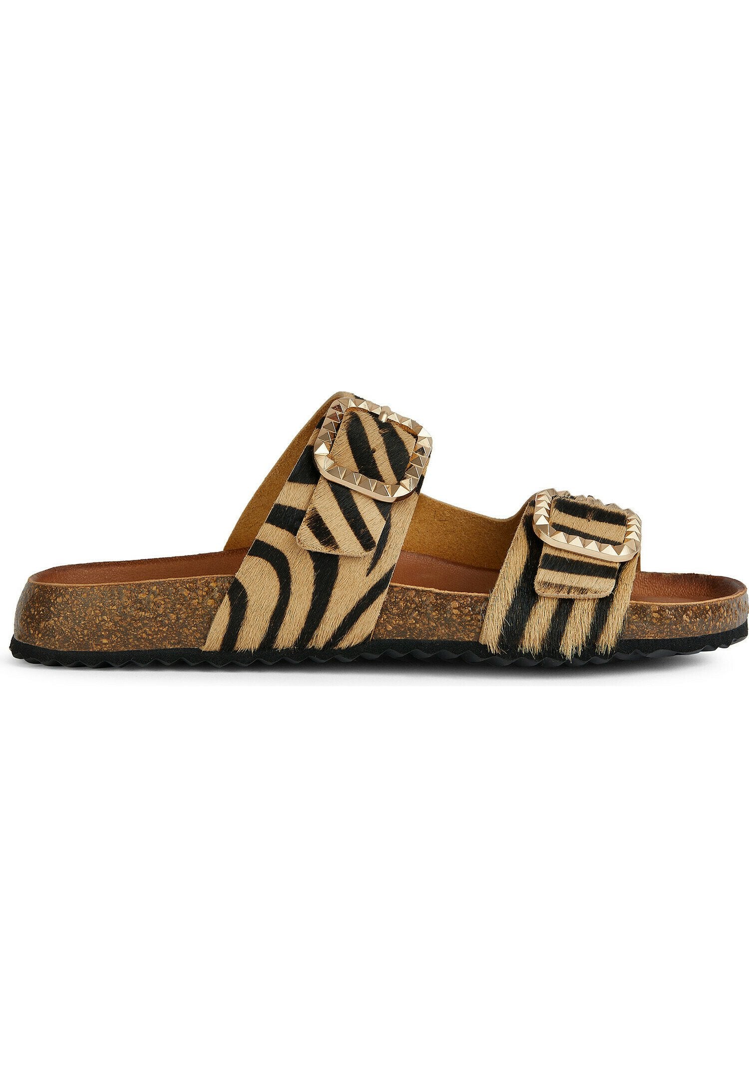 Flache Sandalen mit Obermaterial aus Zebra-Muster-Fell, zwei verstellbaren Riemen mit Pyramidennieten und einer strukturierten Korksohle. Farbgebung in Braun und Schwarz.
