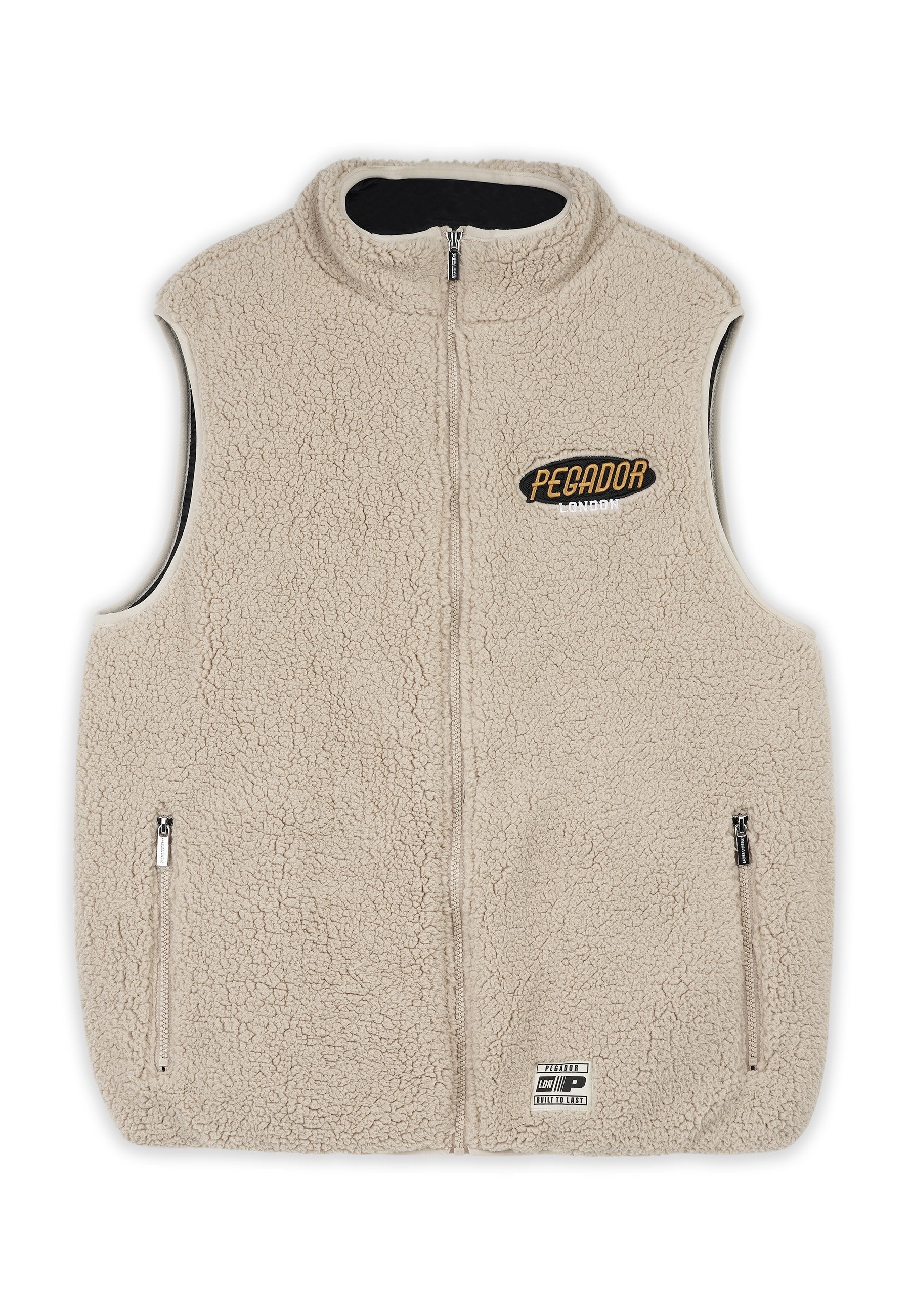 Beige Fleece-Weste mit hohem Kragen, durchgehendem Reißverschluss, zwei Seitentaschen und schwarzem Innenfutter. Merkmale das "PEGADOR"-Logo auf der Brust.