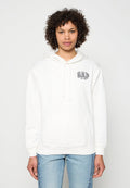 Person mit lockigem Haar, trägt einen weißen GAP-Hoodie mit Fronttasche und hellblauen Jeans, steht vor einem schlichten Hintergrund.